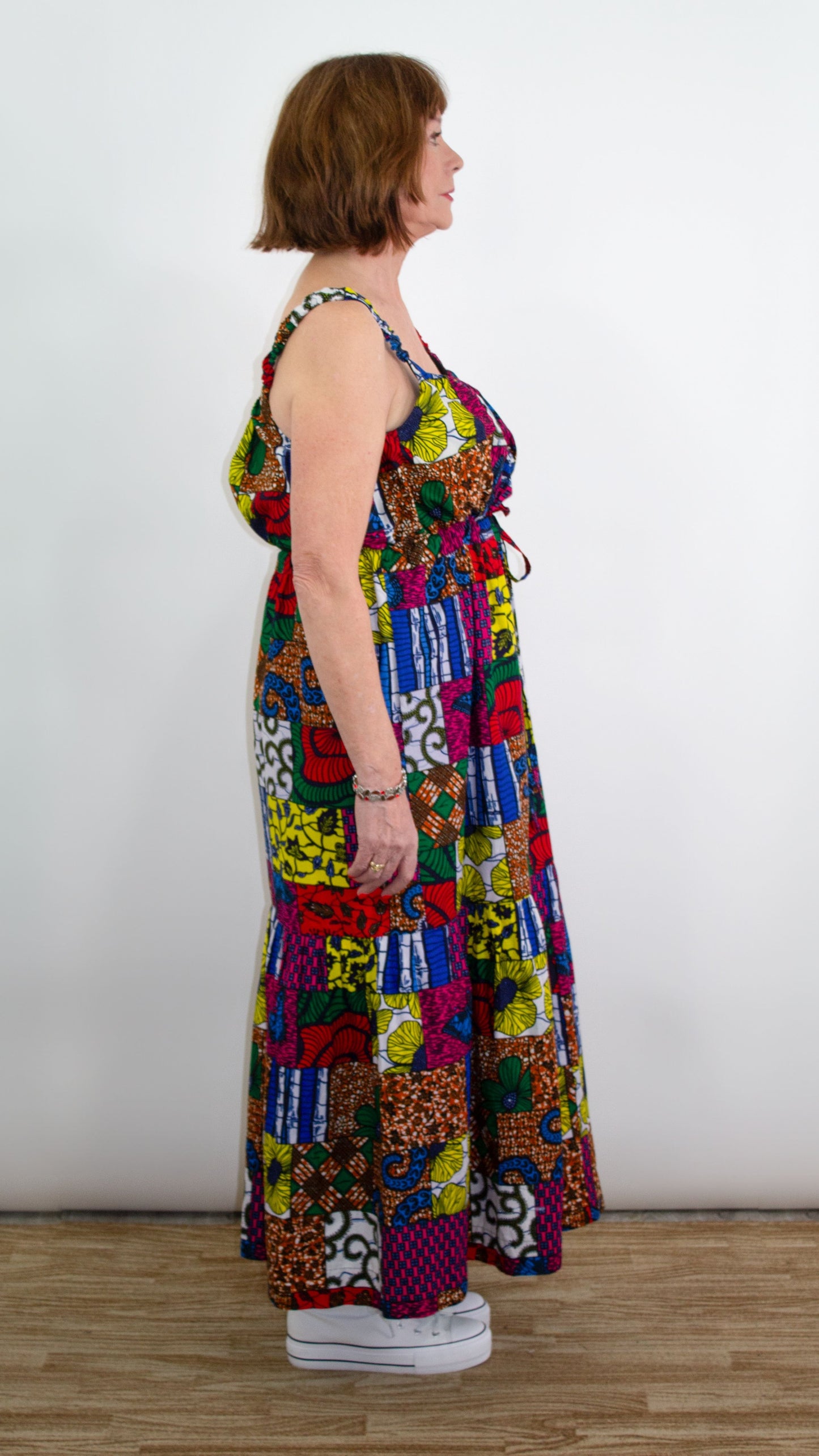 A side profile view of a model striking a pose in a long maxi patchwork dress, showcasing the stylish tie belt and delicate straps.