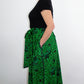 the side of a model wearing the botanical green print skirt paired with a black top and white ballet flats.