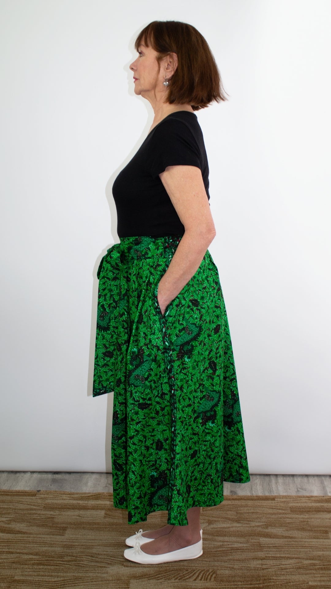 the side of a model wearing the botanical green print skirt paired with a black top and white ballet flats.