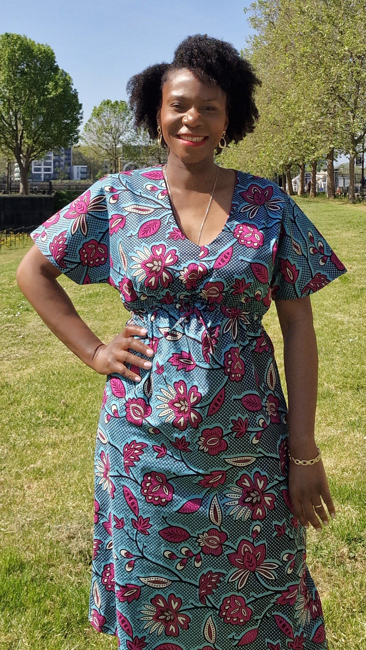 A woman wearing the blue print kaftan dress with pink elements in a park setting, posing confidently.