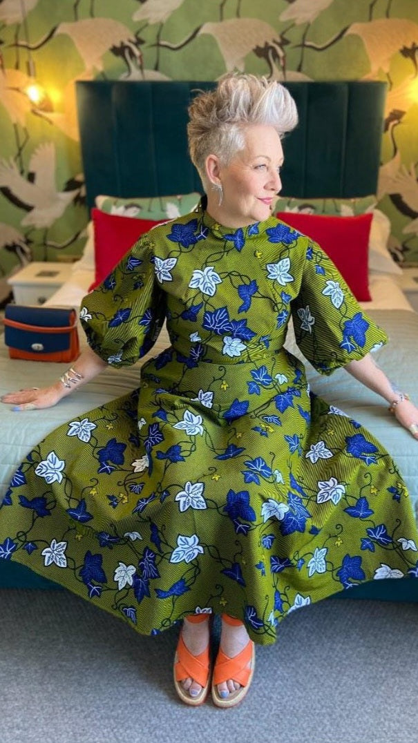 A person sits gracefully in a khaki dress in a room, showcasing the dress's flexibility and openness. Paired with stylish orange sandal platform heels.