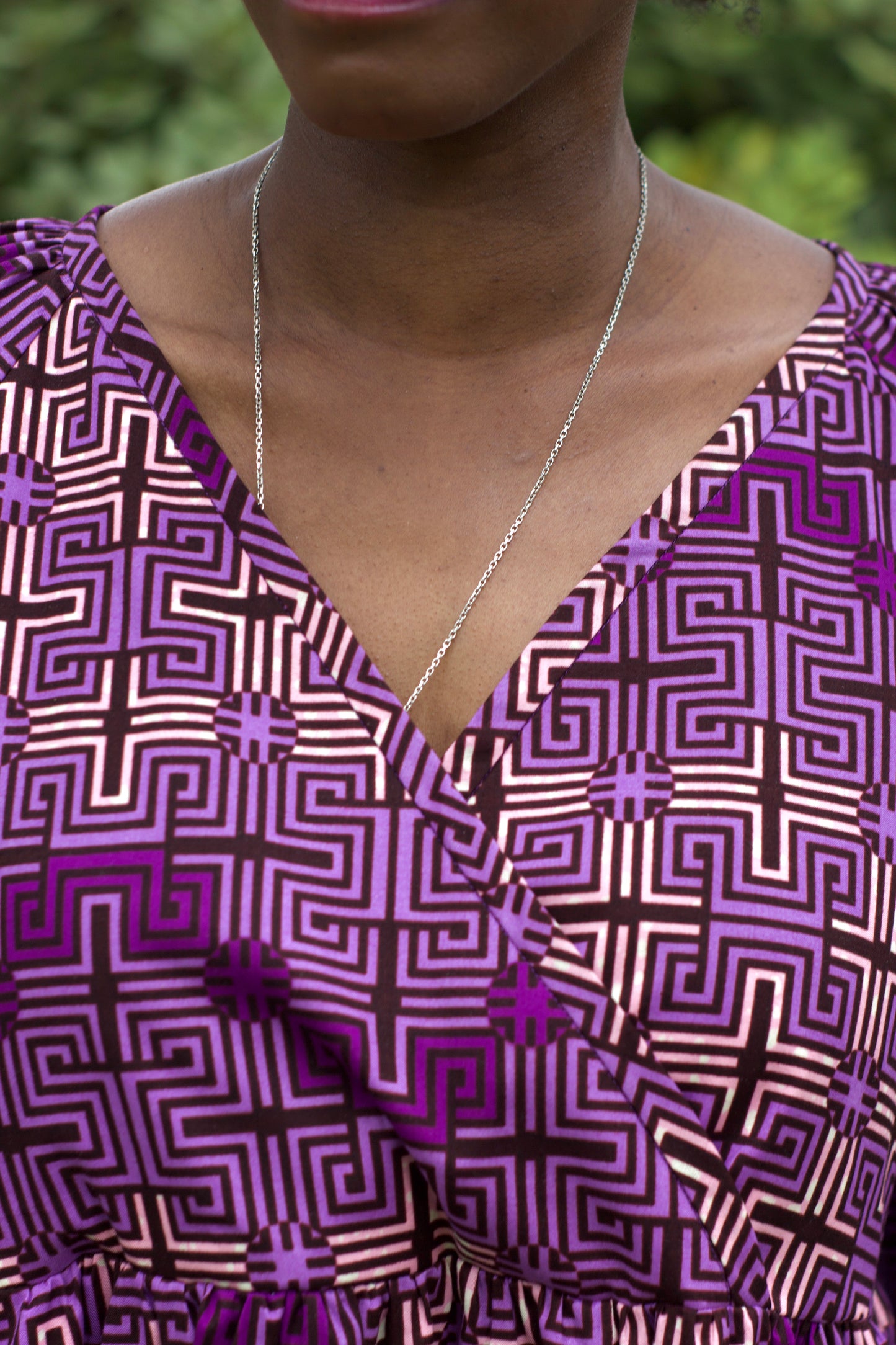 Close up of purple ruffle print dress neck line, paired with a silver long necklace.