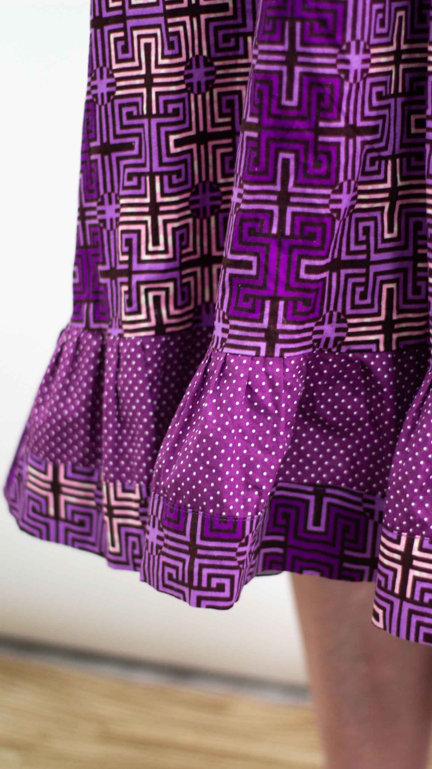 A close-up view accentuating the ruffle effect of the dress, particularly showcasing the point where the fabric print transitions into a purple line with white polka dots.