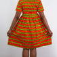 A model elegantly reveals the back of a short orange-yellow striped print dress, gracefully holding and lifting the dress to showcase its charming details. 