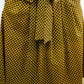model posing with hands in pockets to showcase the details of a yellow African print skirt, featuring a tie belt skillfully tied in a trendy and elegant bow. The ensemble is completed with chic black ballet flats.