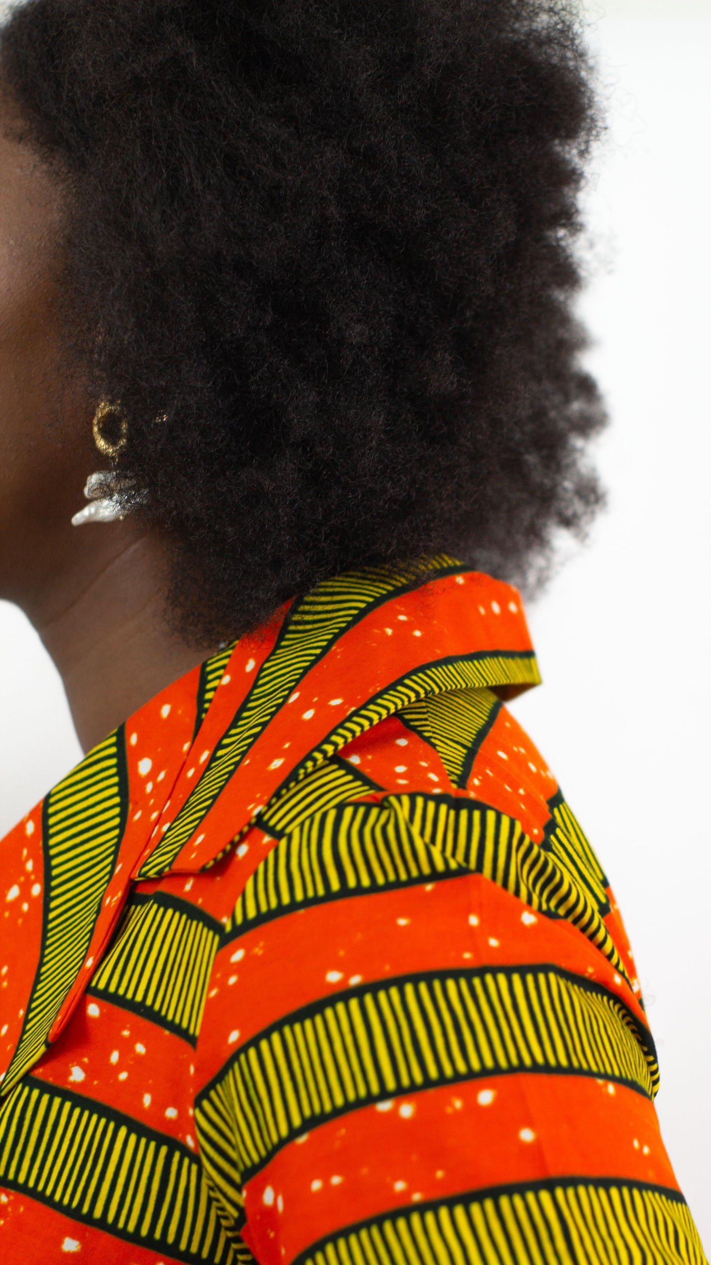 A close-up view capturing the intricate details of a V-neck orange-striped African print dress, paired with golden earrings.