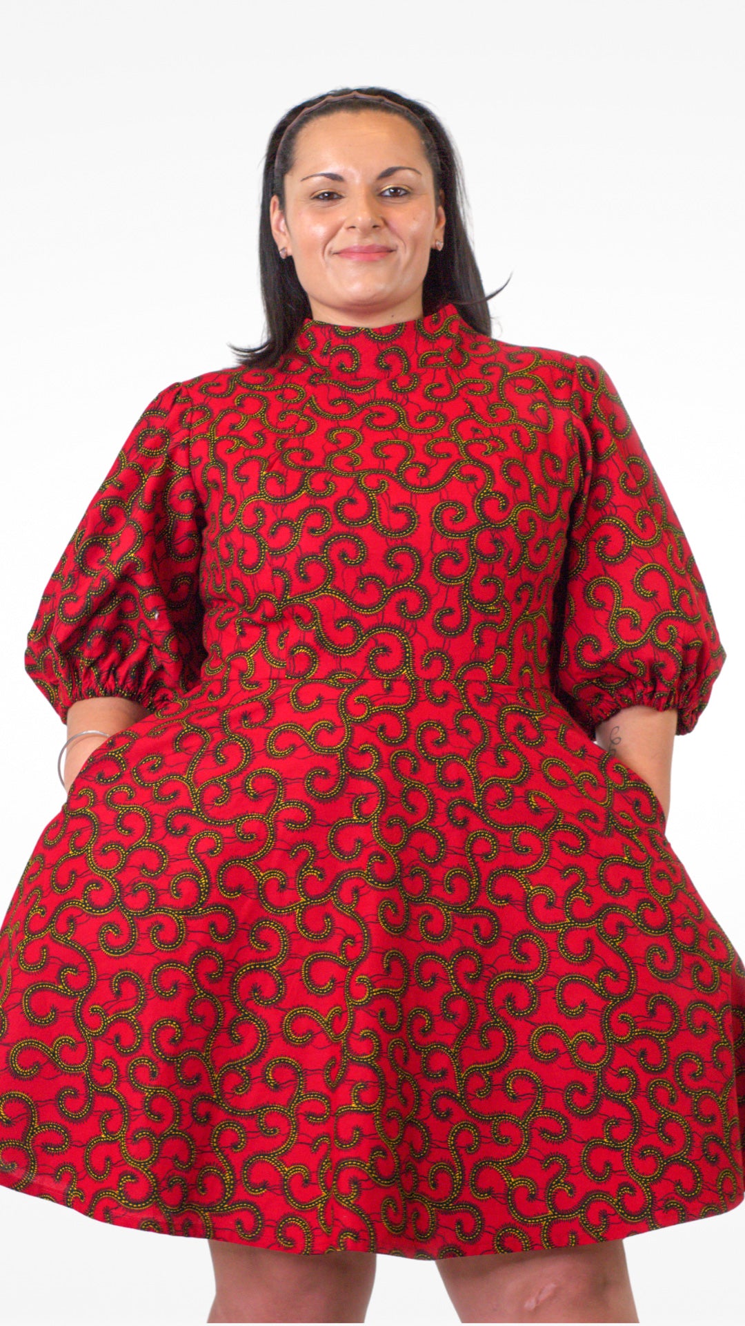 A close up of model in a short red print puff sleeve dress, having placed her hands in pockets.