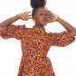 A woman confidently strikes a pose with arms up, showcasing the intricate elements of the neckline of her orange print puff sleeve dress.