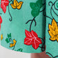 A close up of the red, green and orange leaf design elements of the green fabric print dress.