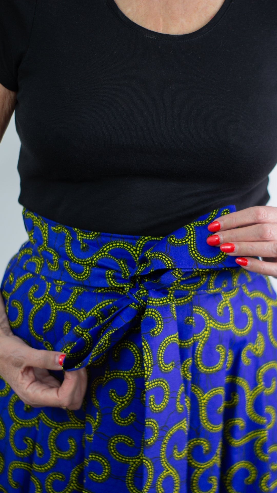 A close-up view capturing the details of a swirly blue print skirt with golden elements, featuring a tie belt skilfully tied in a trendy and elegant bow. 