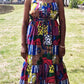 A woman posing with a radiant smile in a maxi long print patchwork dress, adorned with jewellery, in a park setting.