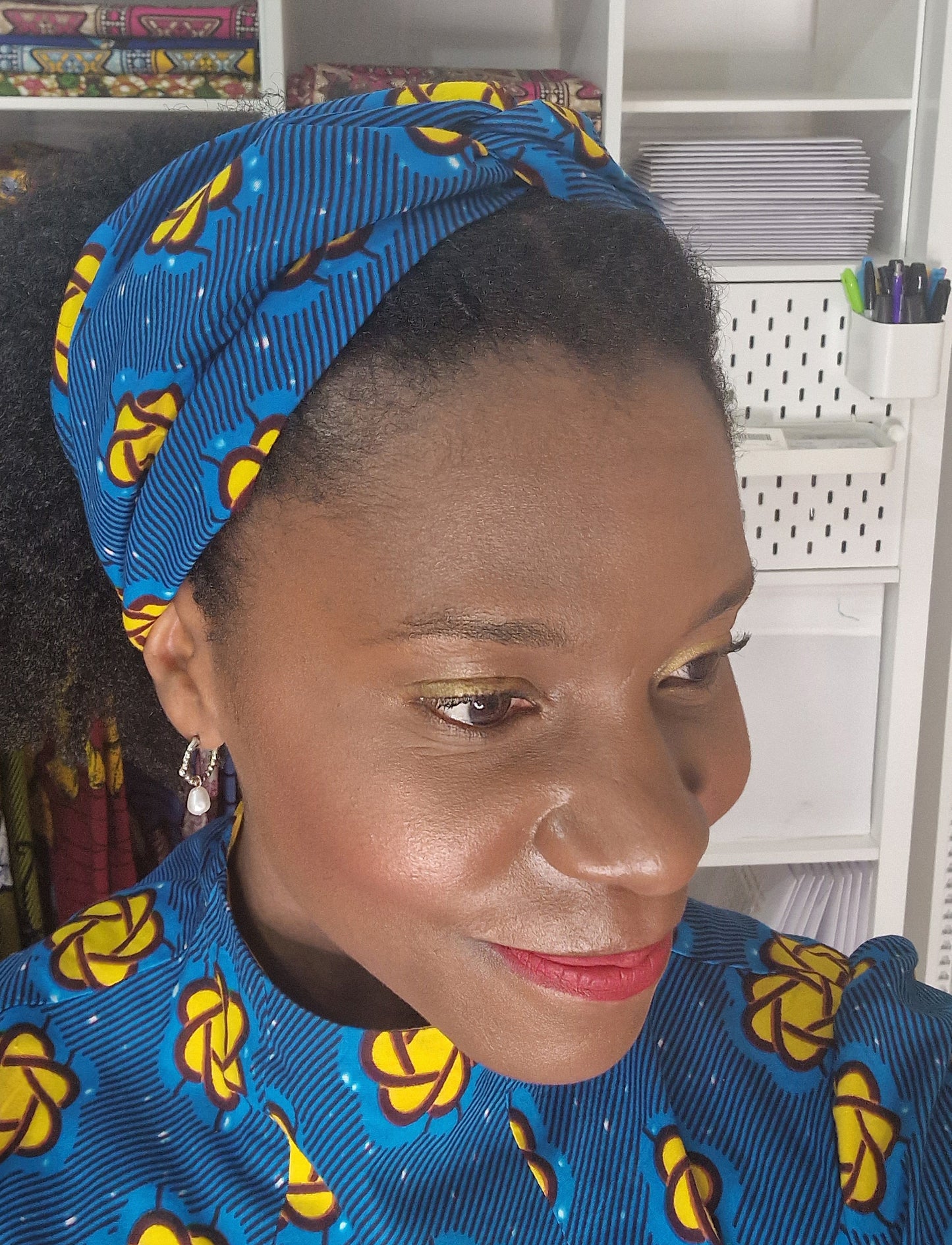 A close-up of a woman wearing a blue and yellow headband with matching blue and yellow print dress.