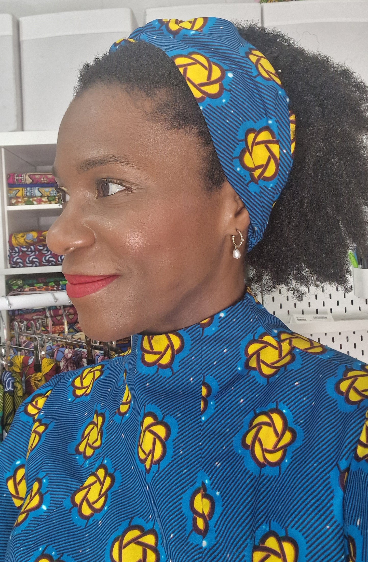 A side close up of a woman wearing a blue and yellow headband with matching blue and yellow print dress.