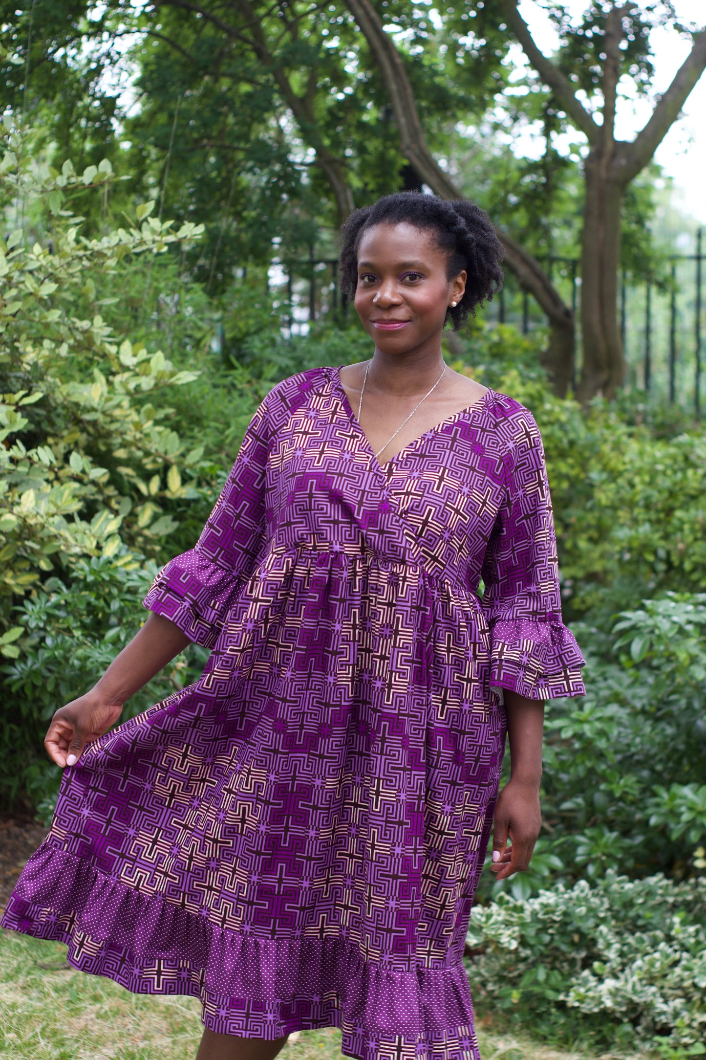 A woman playfully posing with the purple print ruffle dress, showcasing its flowing nature and elegance, while surrounded by nature.
