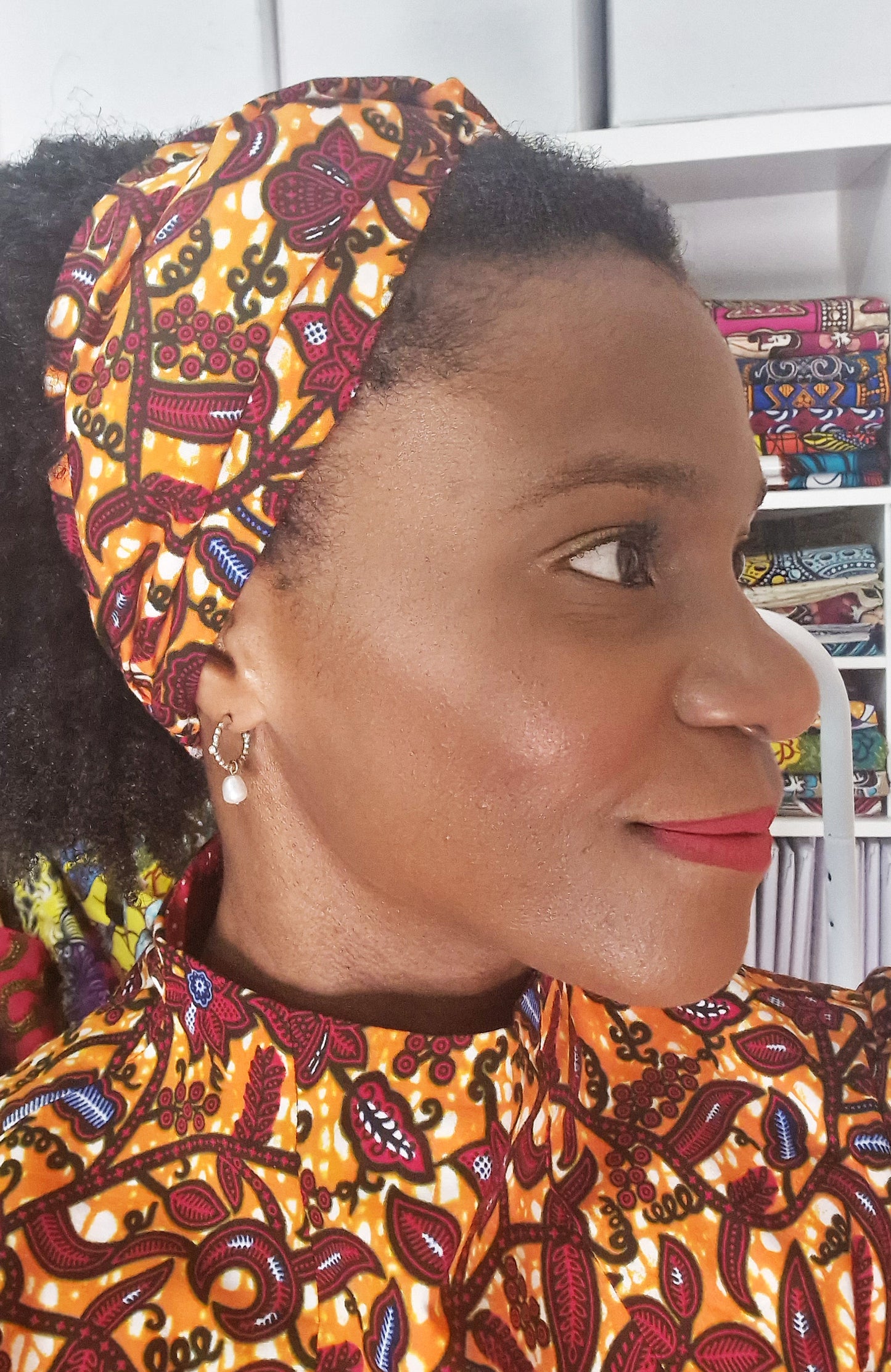 A close up of a woman wearing the orange patterned headband and a matching print dress.