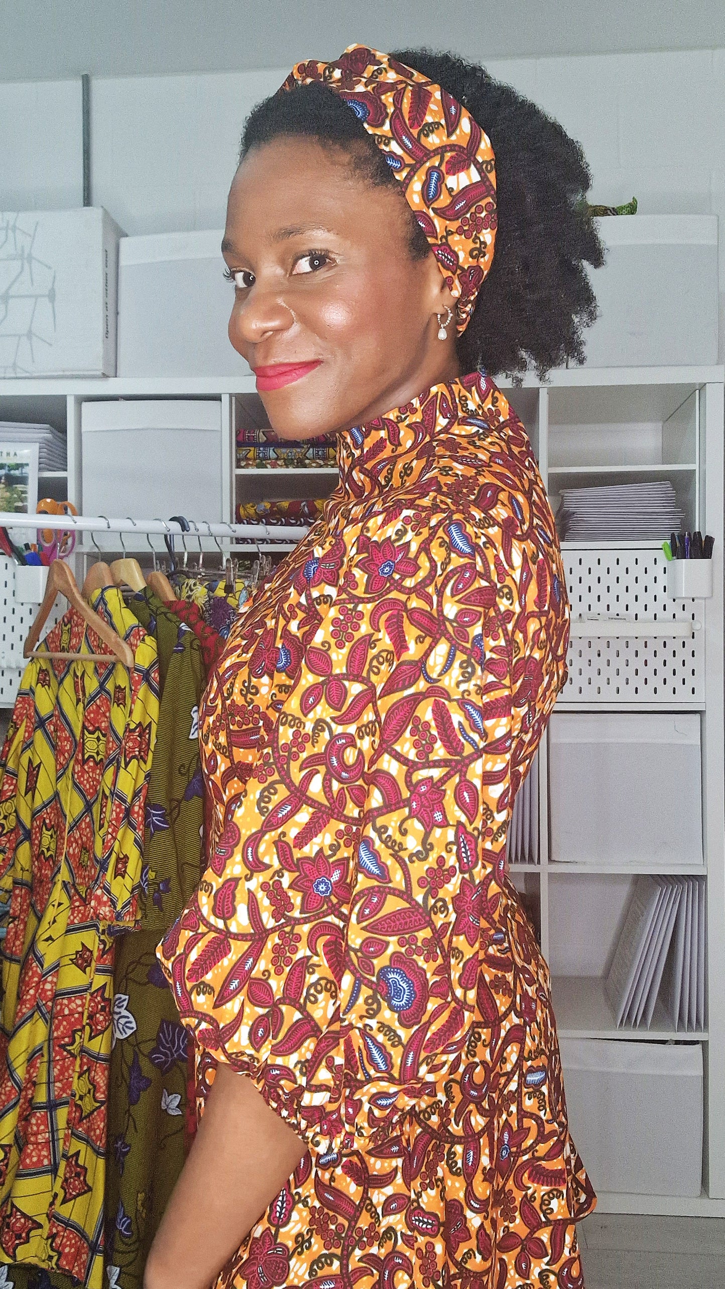 A side view of a woman wearing the orange patterned headband in a matching print dress.