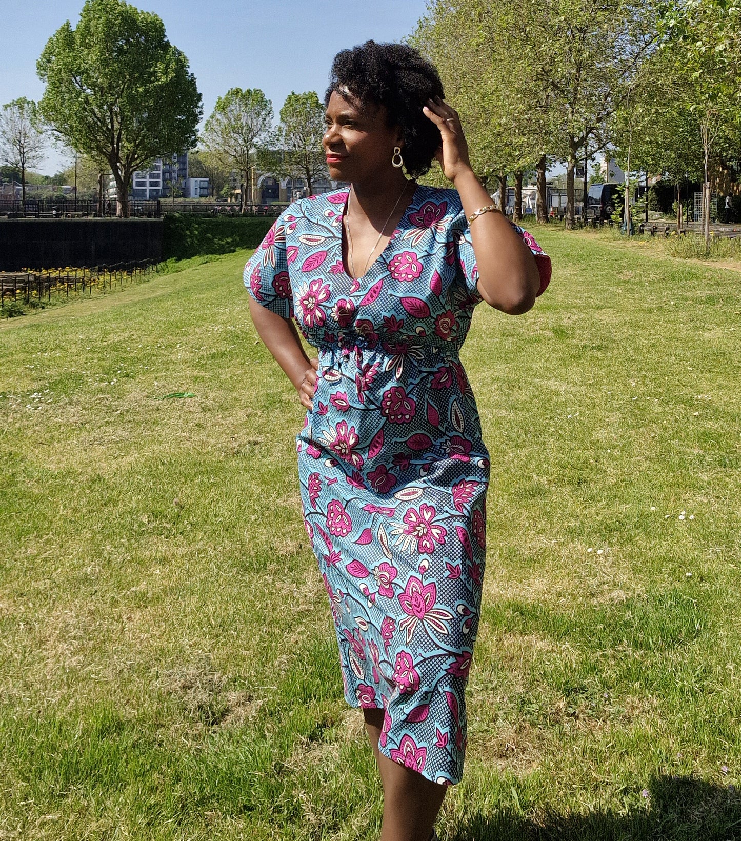 A woman strikes a pose in a stylish blue kaftan dress adorned with a pink floral print in a park.. 