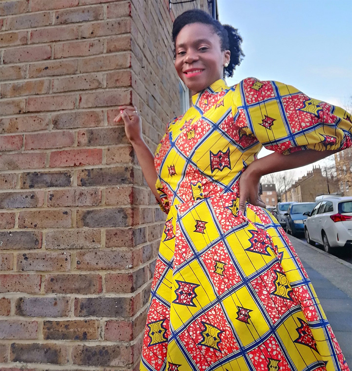 a person in a yellow puff sleeve dress leaning against a brick wall, showcasing the fitted waistline of the dress.
