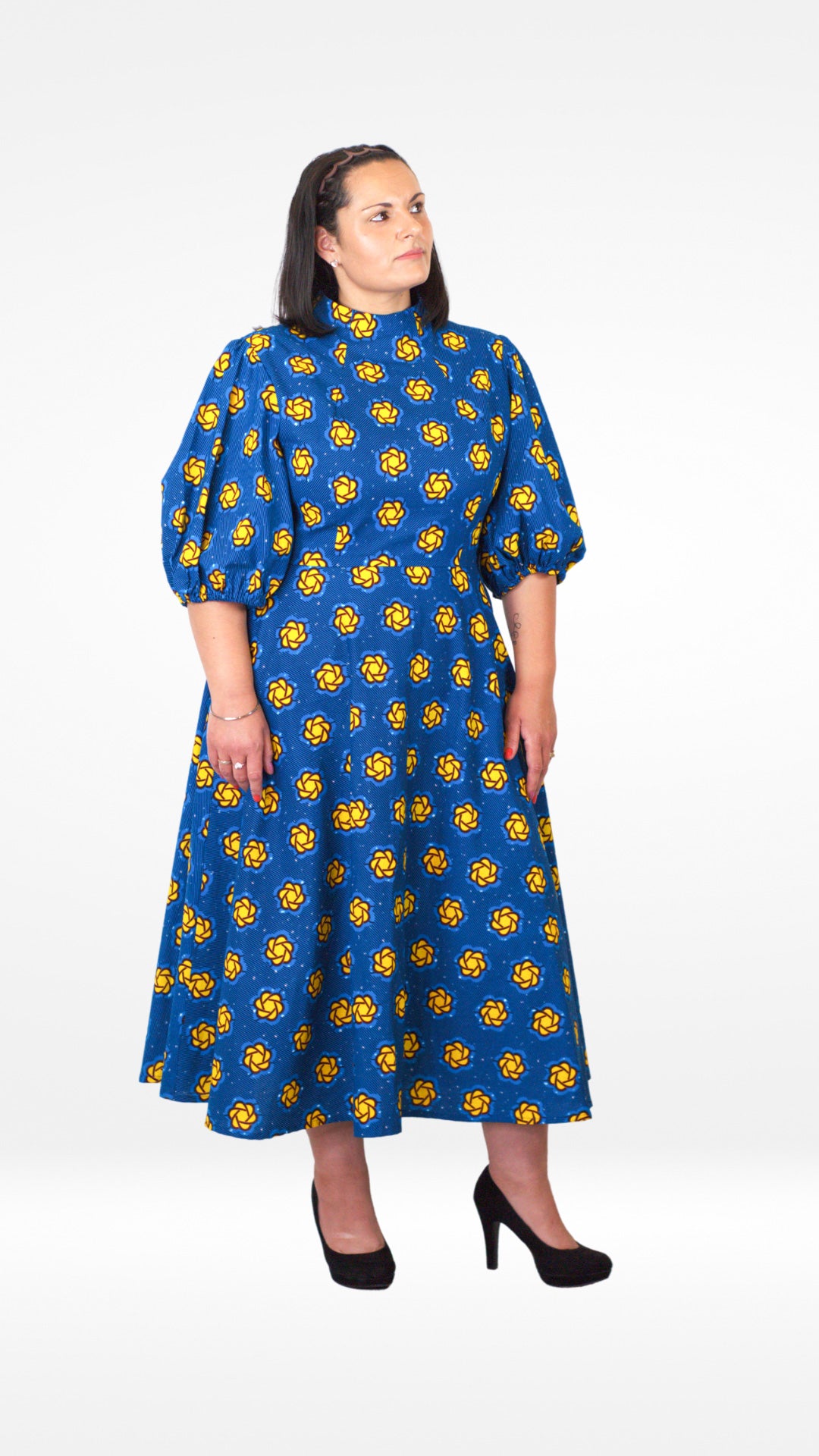 A model poses in a blue puff sleeve long dress with playful yellow elements and paired with black classic heels.