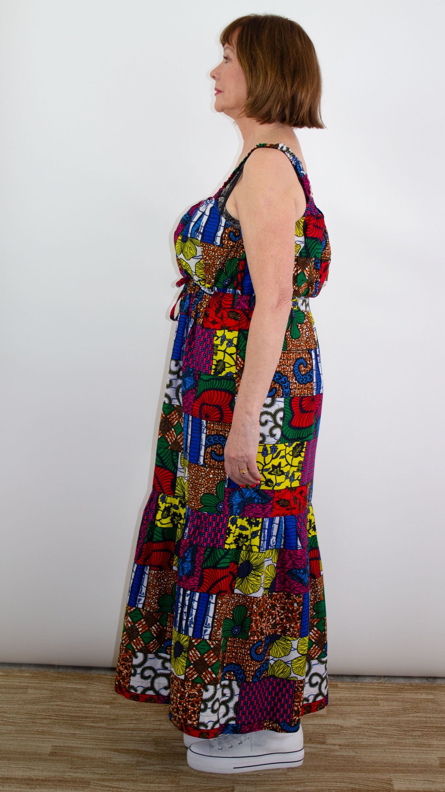 A side profile view of a model striking a pose in a long maxi patchwork dress, showcasing the stylish tie belt and delicate straps.