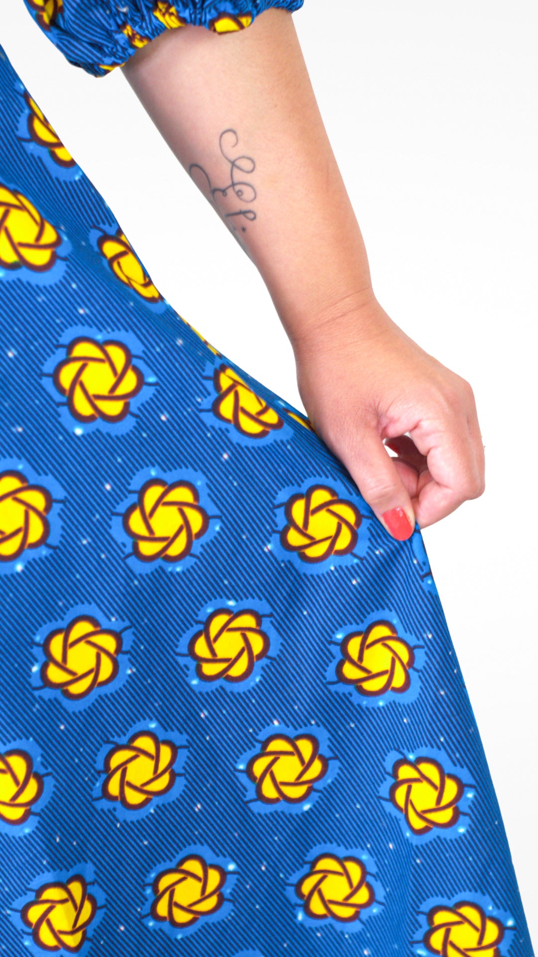 A close-up of a person's hand delicately holding the blue dress, emphasizing the fabric's texture and the beautiful yellow elements.