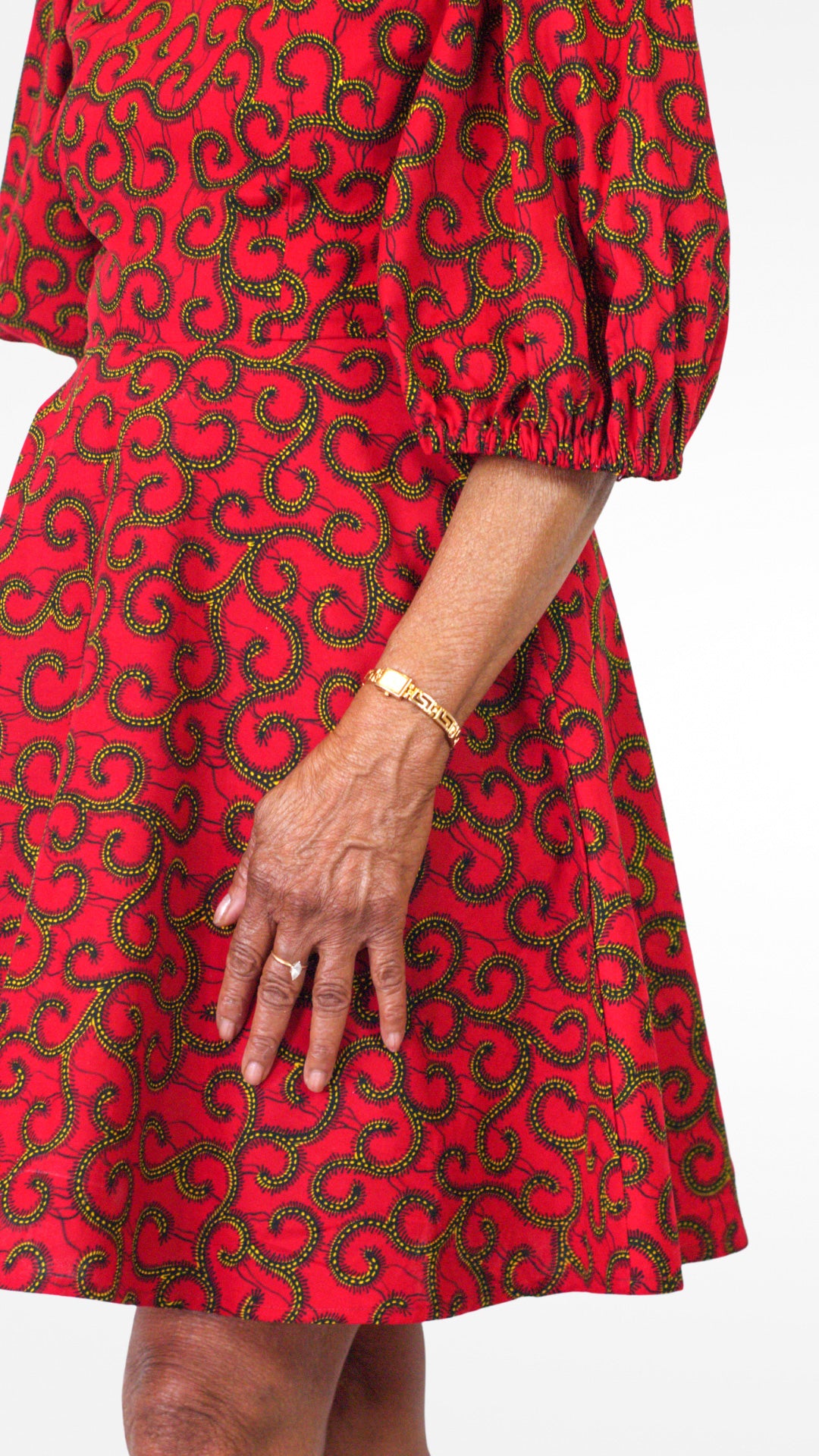 A close-up of model's hand placed on the red dress, adding a personal touch and showcasing the fabric's texture and design details.