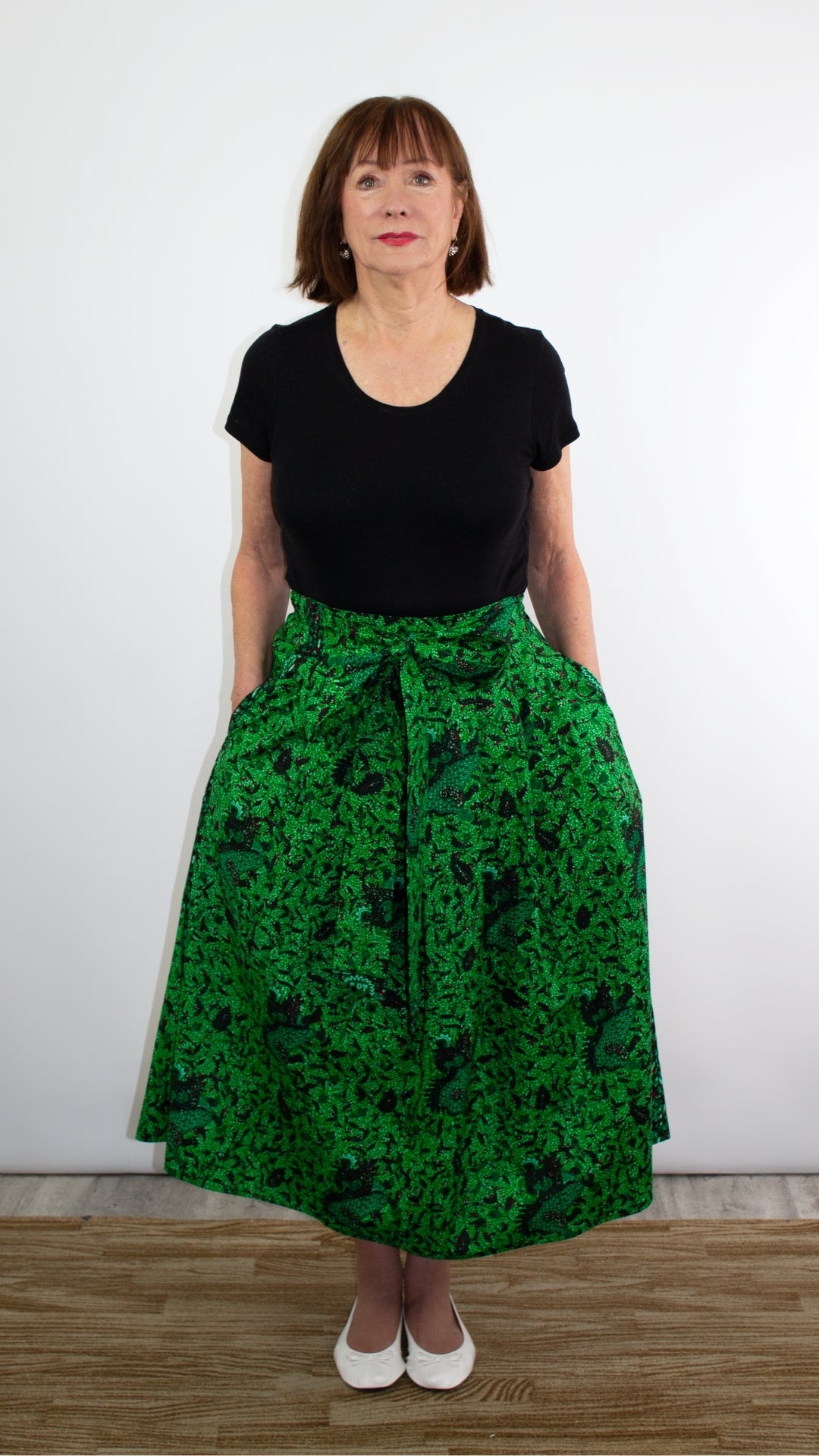 A model adorned in a botanical green print skirt creates a vibrant and eye-catching look. The green hue paired with a black top and white ballet flats adds a refreshing touch to the ensemble, showcasing a blend of fashion and individual flair.