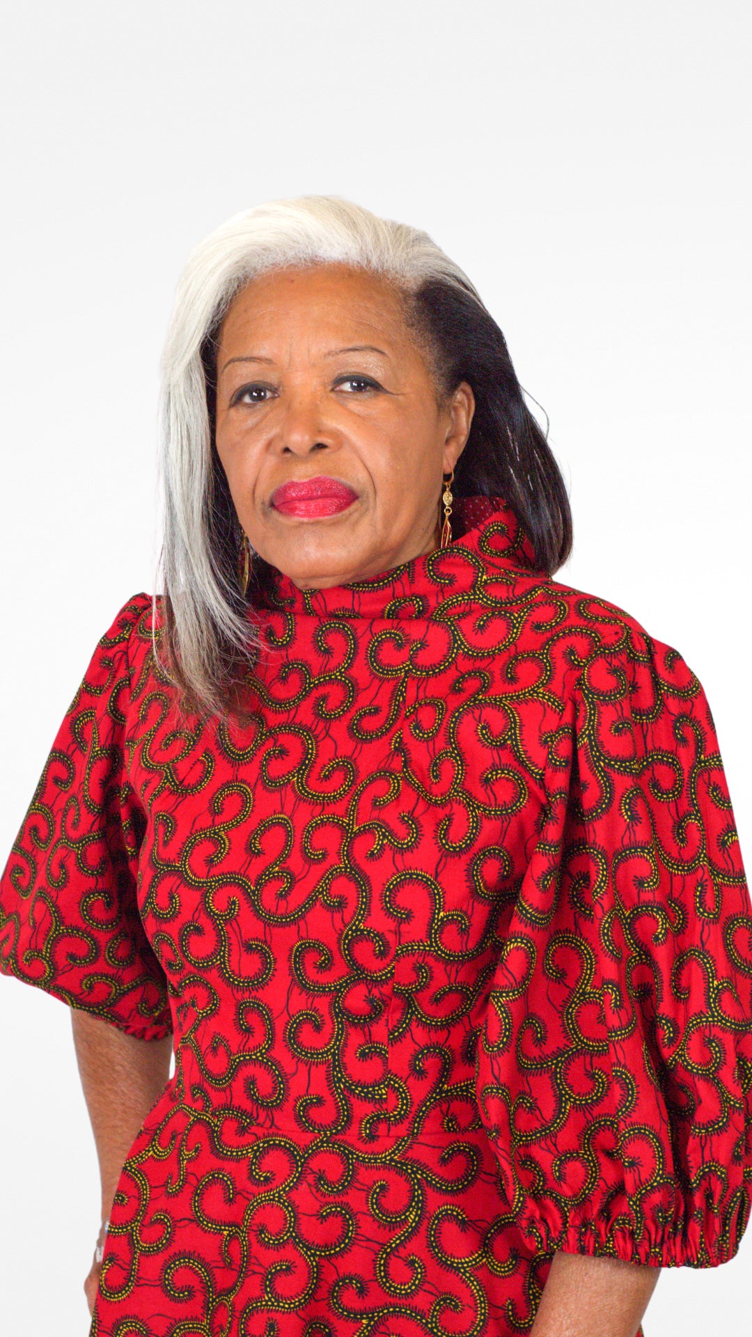 Close up of model's face, showcasing the swirly details, neckline and puff sleeves of the red print dress.