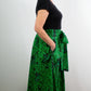 Model showcasing the side look of a botanical green print skirt with hands in pockets.