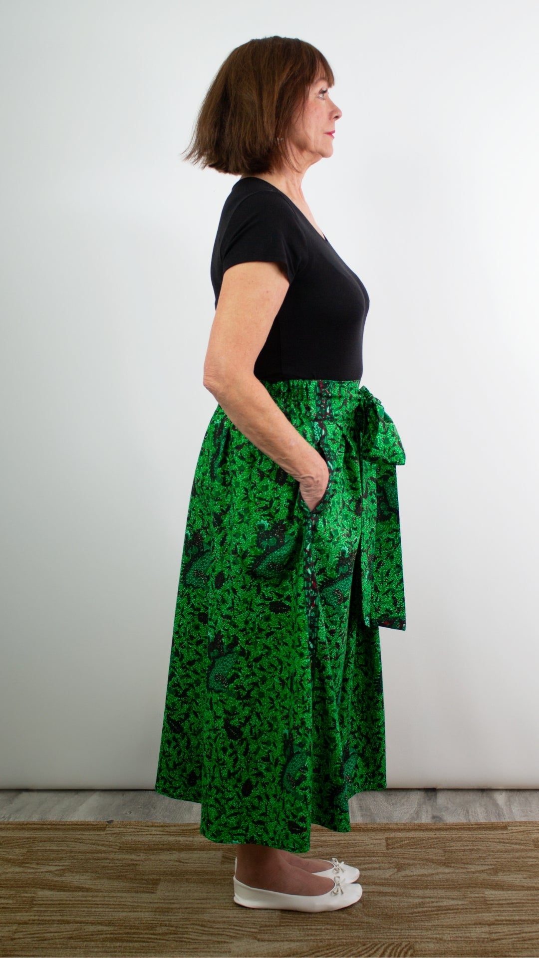Model showcasing the side look of a botanical green print skirt with hands in pockets.