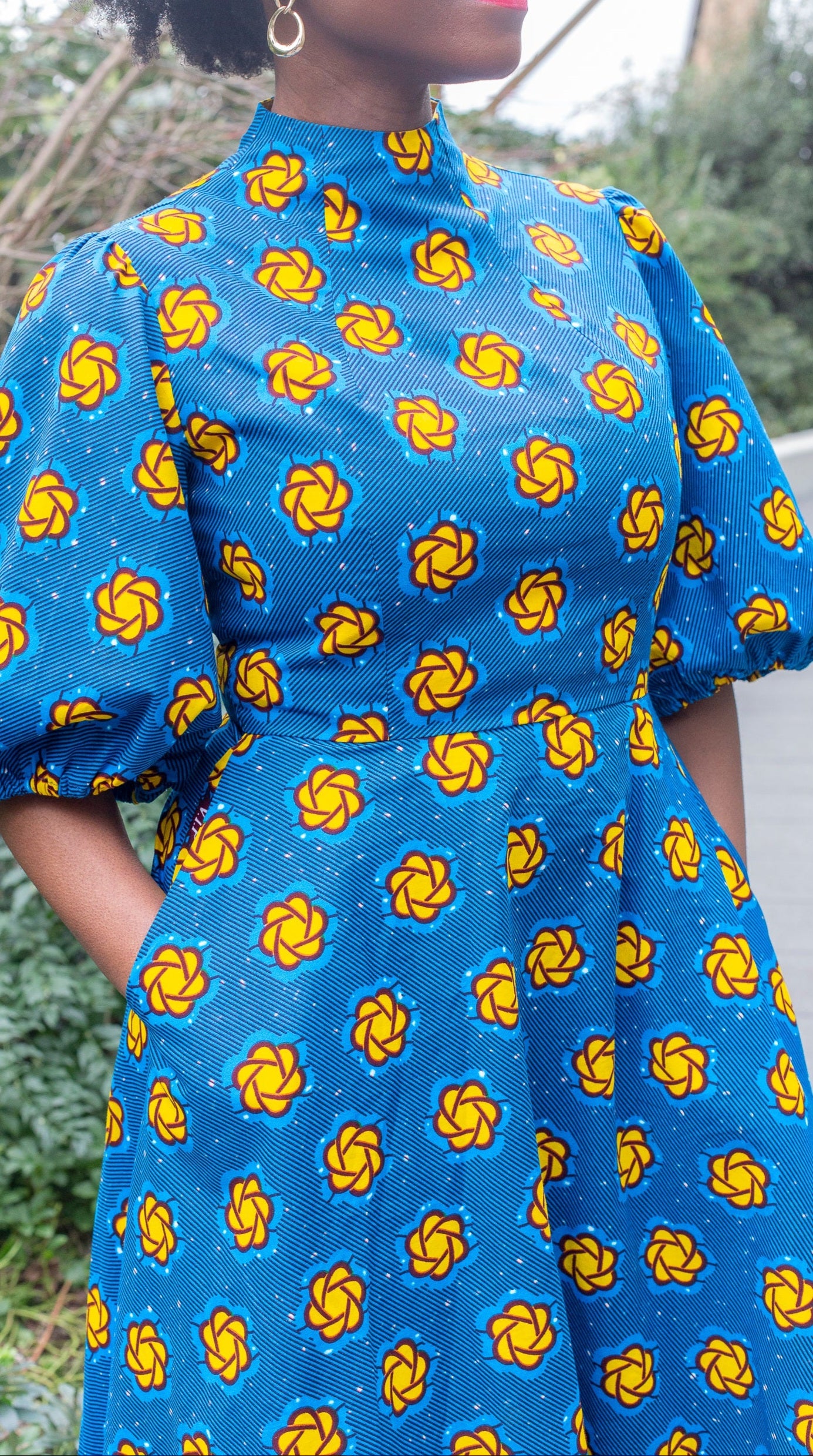 A close up of the yellow details, fitted waistline, high neck and puff sleeves of the blue print dress.