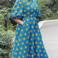 A woman posing with a smile in the long blue print puff sleeve dress in a park setting.