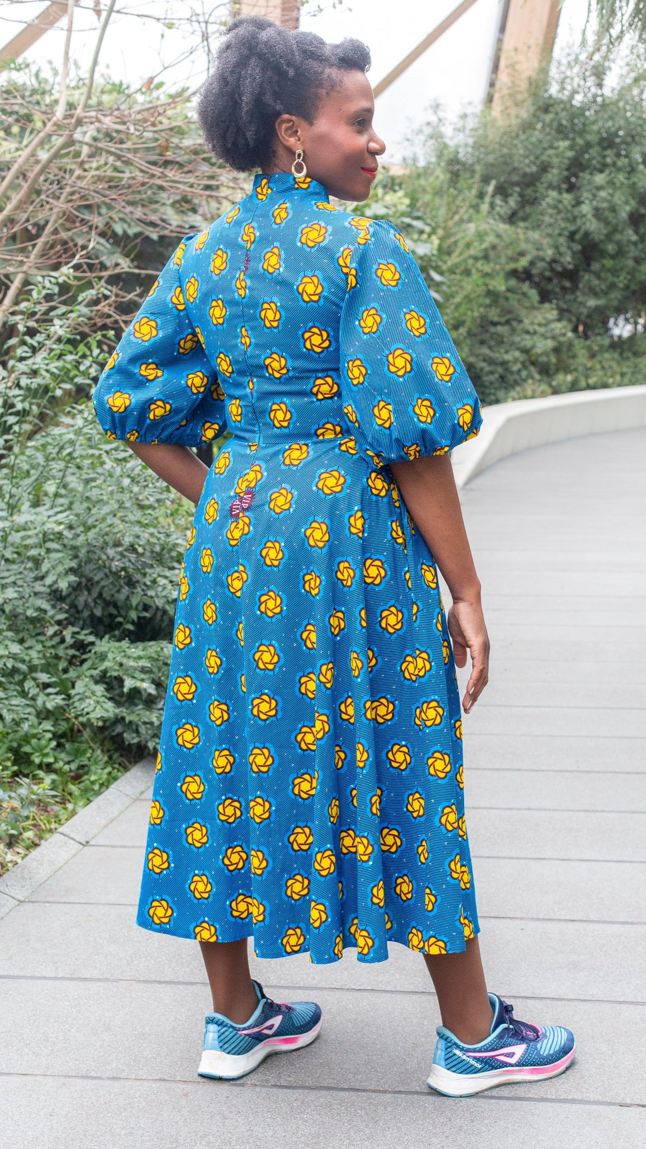 A woman showcasing the back of the long puff sleeve blue print dress in a park setting.