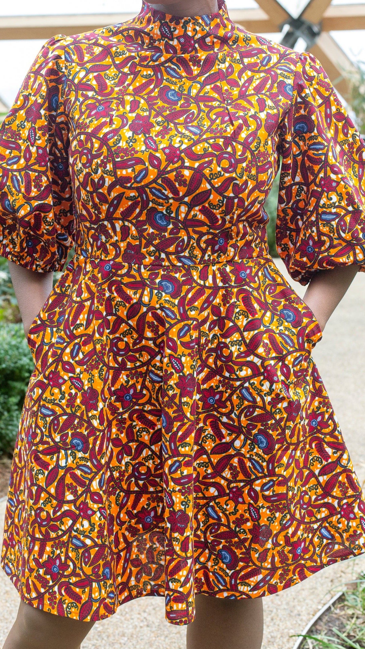 A vibrant orange puff sleeve short dress with detailed blue and red floral elements and fitted waistline.