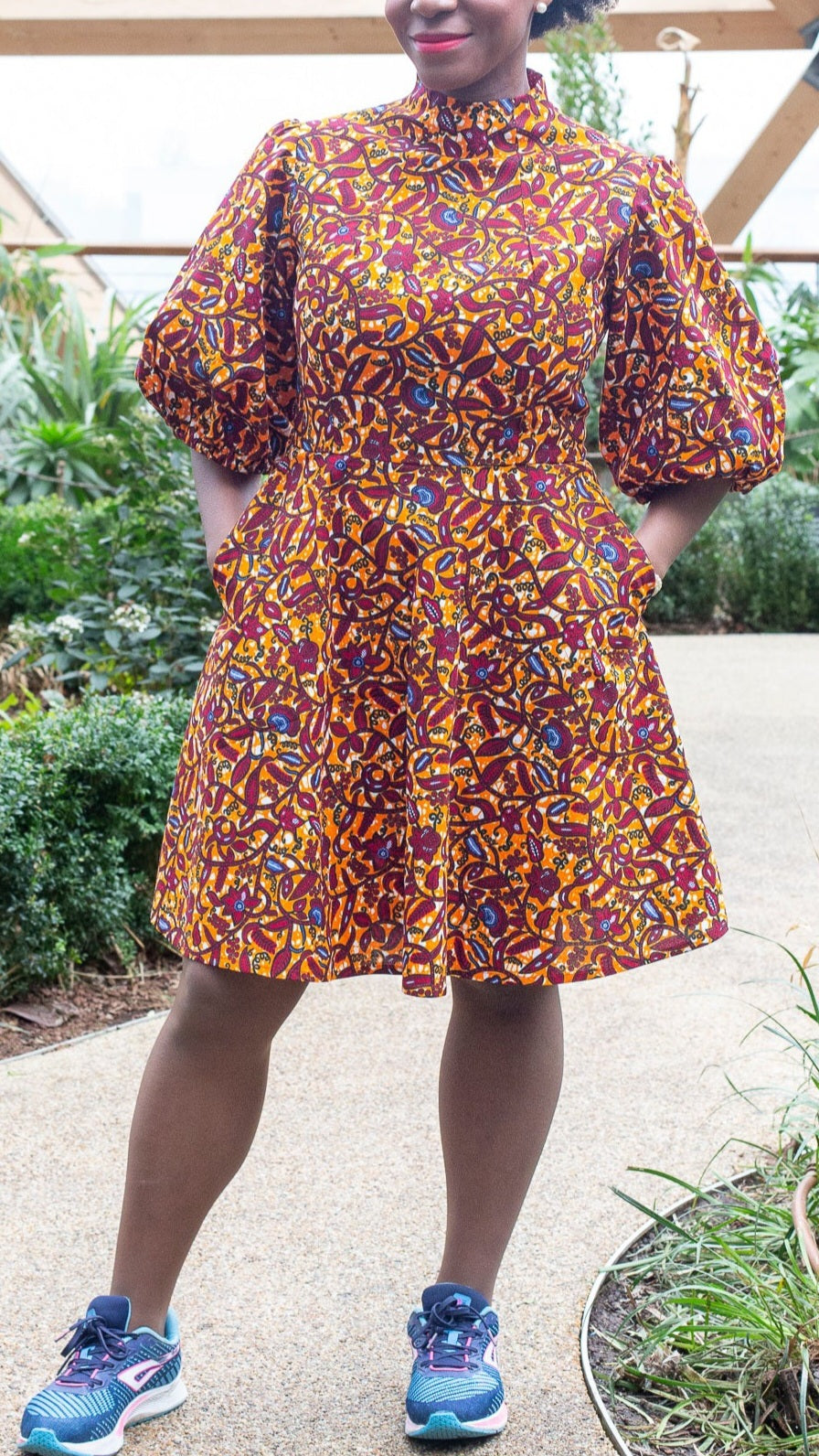 A woman wearing the short orange print puff sleeve dress, paired with blue trainers for casual style.