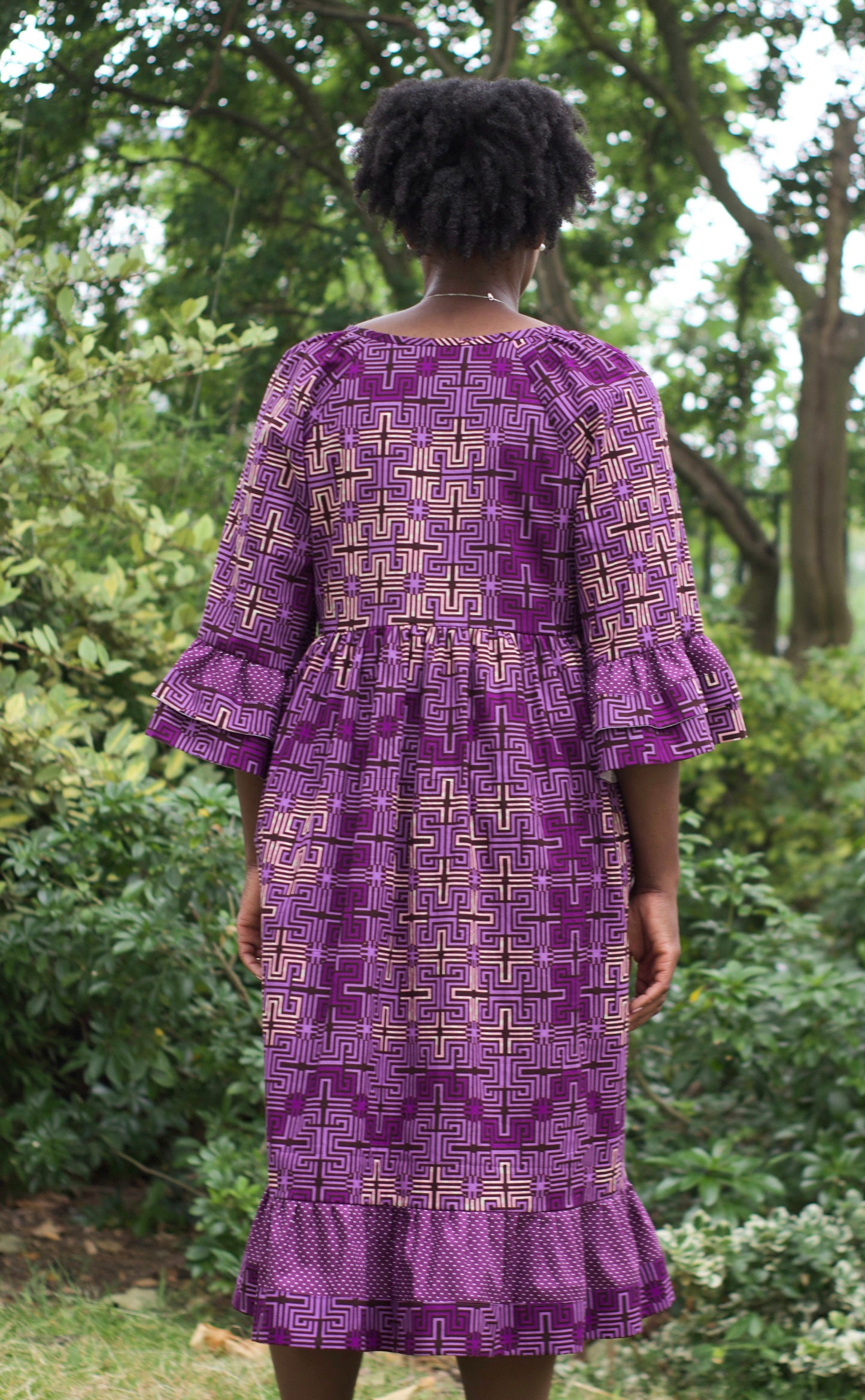 A woman gracefully wearing a purple ruffle dress, her hair elegantly gathered up, in a picturesque park setting.