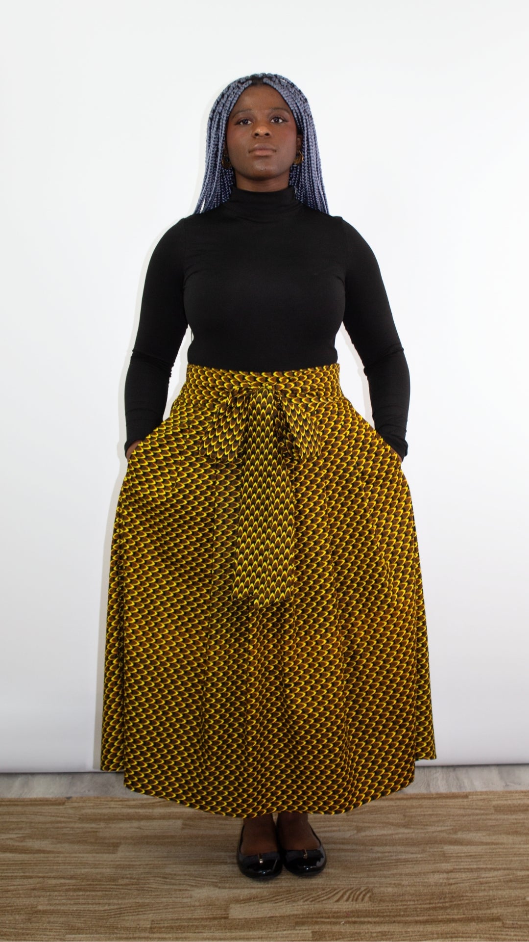 An edgy and stylish model with striking blue hair wearing a sleek black turtleneck paired with a statement yellow and black skirt adorned with a fashionable bow tie belt. The combination of bold colours and modern design creates a unique and eye-catching look.