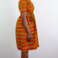 A model standing from the side reveals the tie bow belt of a short orange-yellow striped print dress.