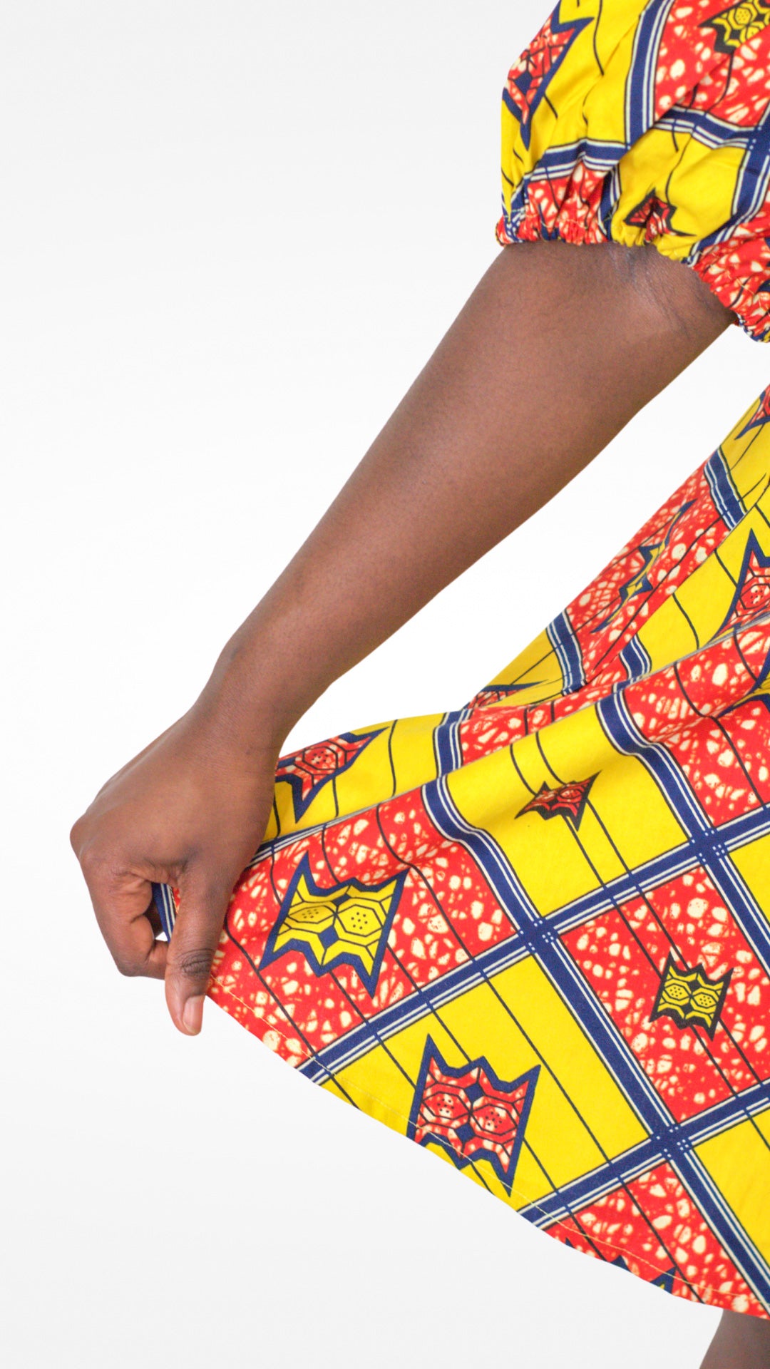 A close-up of a person's hand delicately holding the dress, highlighting the fabric and design details in a graceful manner.