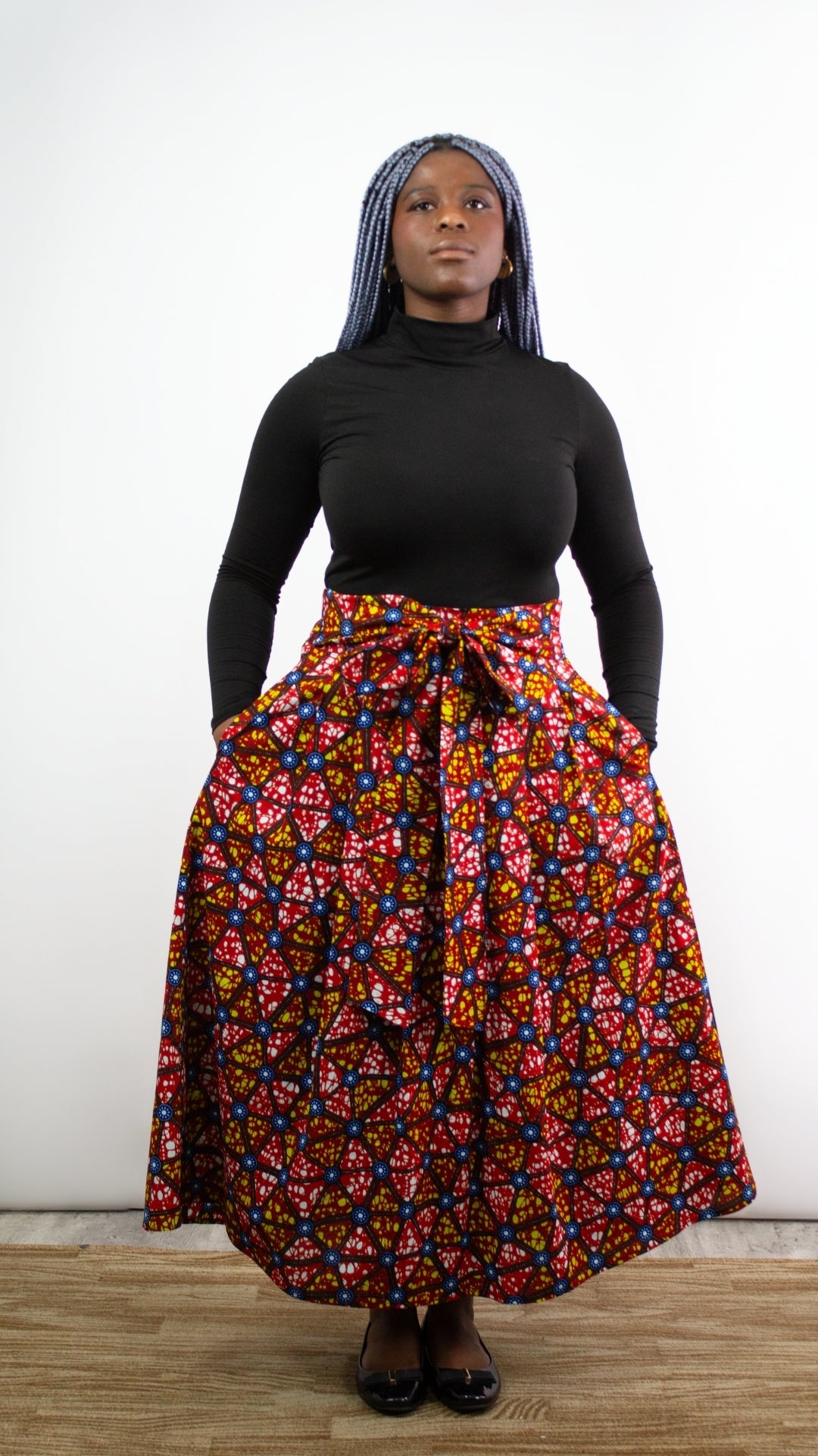A model with blue hair posing standing in a mosaic print long skirt. The bold and artistic patterns of the mosaic print complement the model's unique style, creating a visually captivating and fashion-forward ensemble.