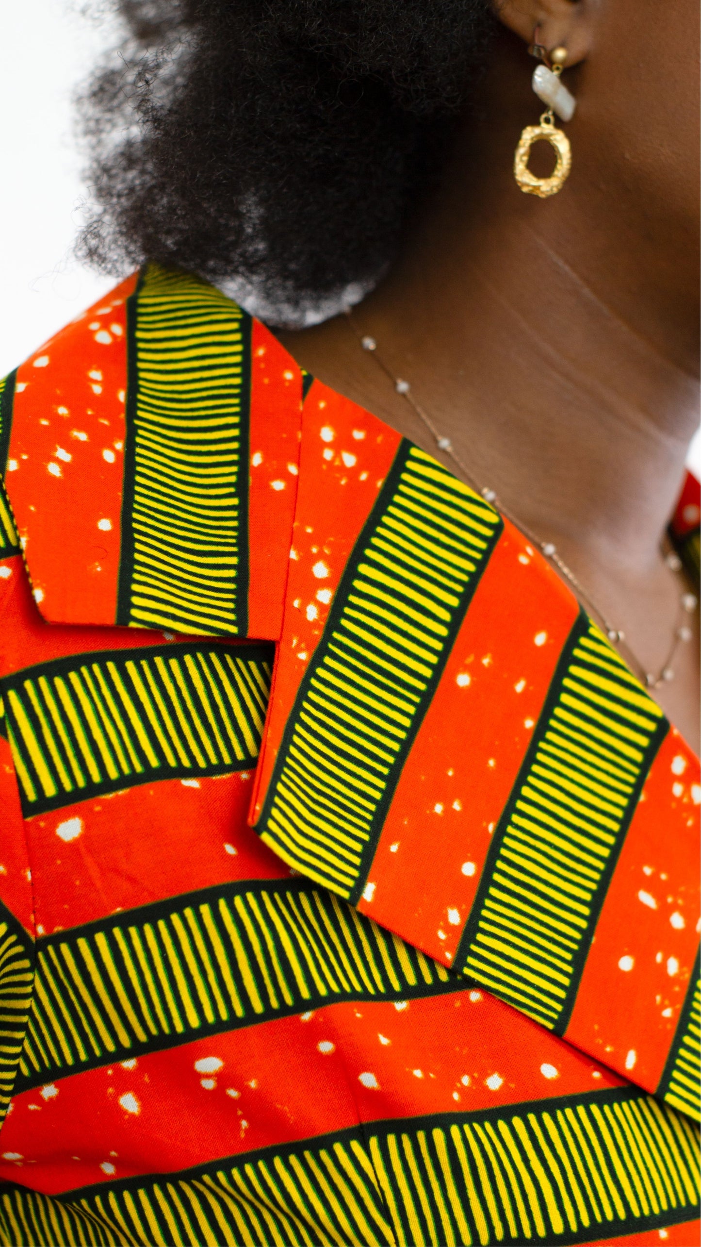 A close up showing the beautiful details of an orange striped print dress, paired with an elegant necklace.