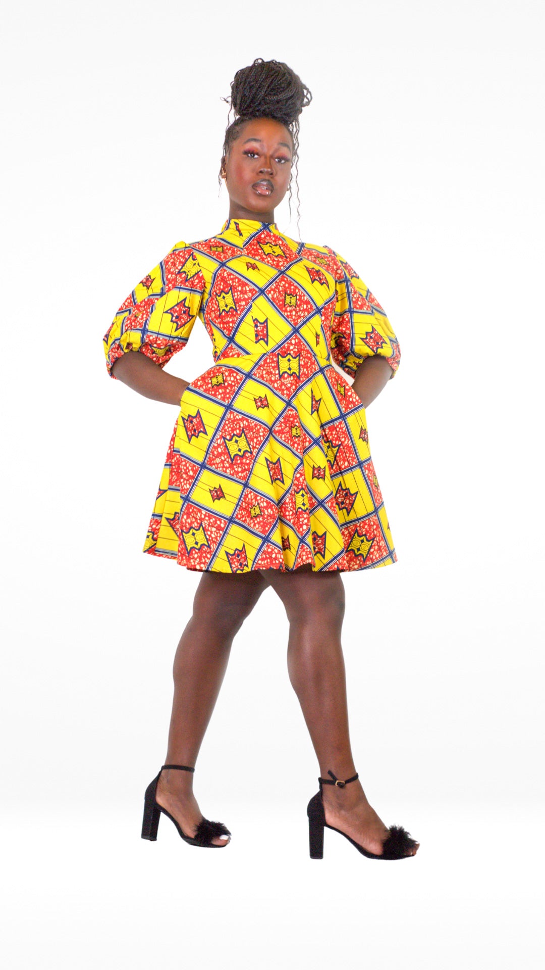 A model posing confidently in a yellow and red short puff-sleeve dress, elegantly paired with black heels and her hair styled up. 