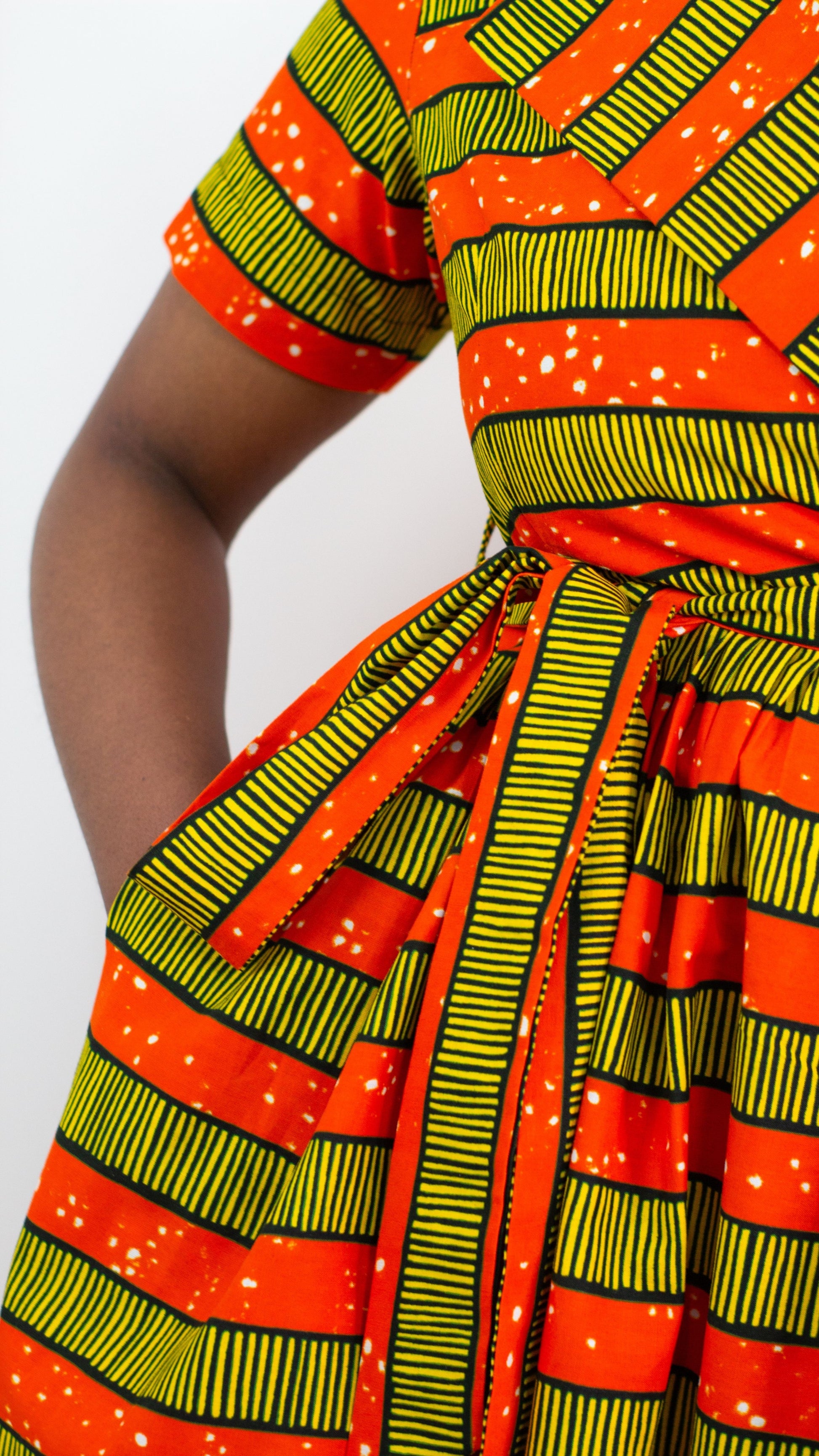A captivating orange-yellow striped print dress featuring practical and stylish pockets. The combination of vibrant colours and functional design.