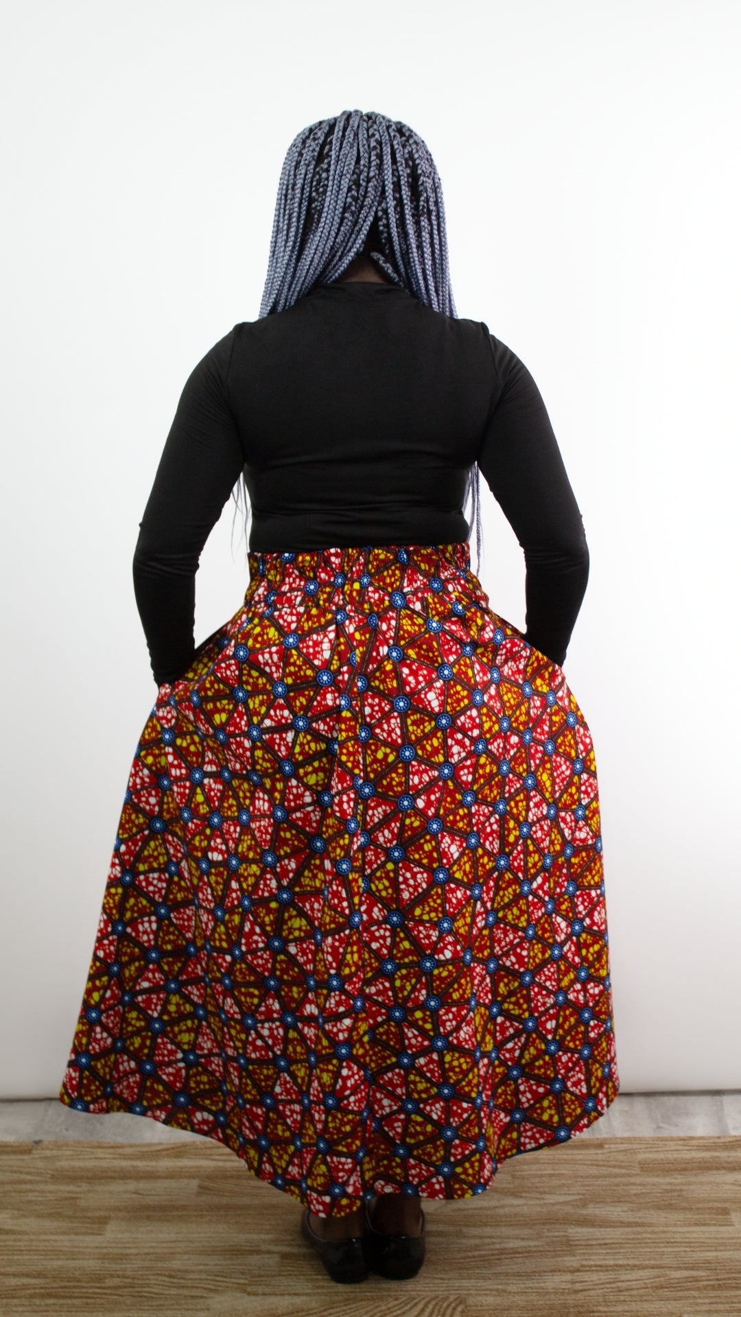 the back of a model with blue hair posing standing in a mosaic print long skirt.