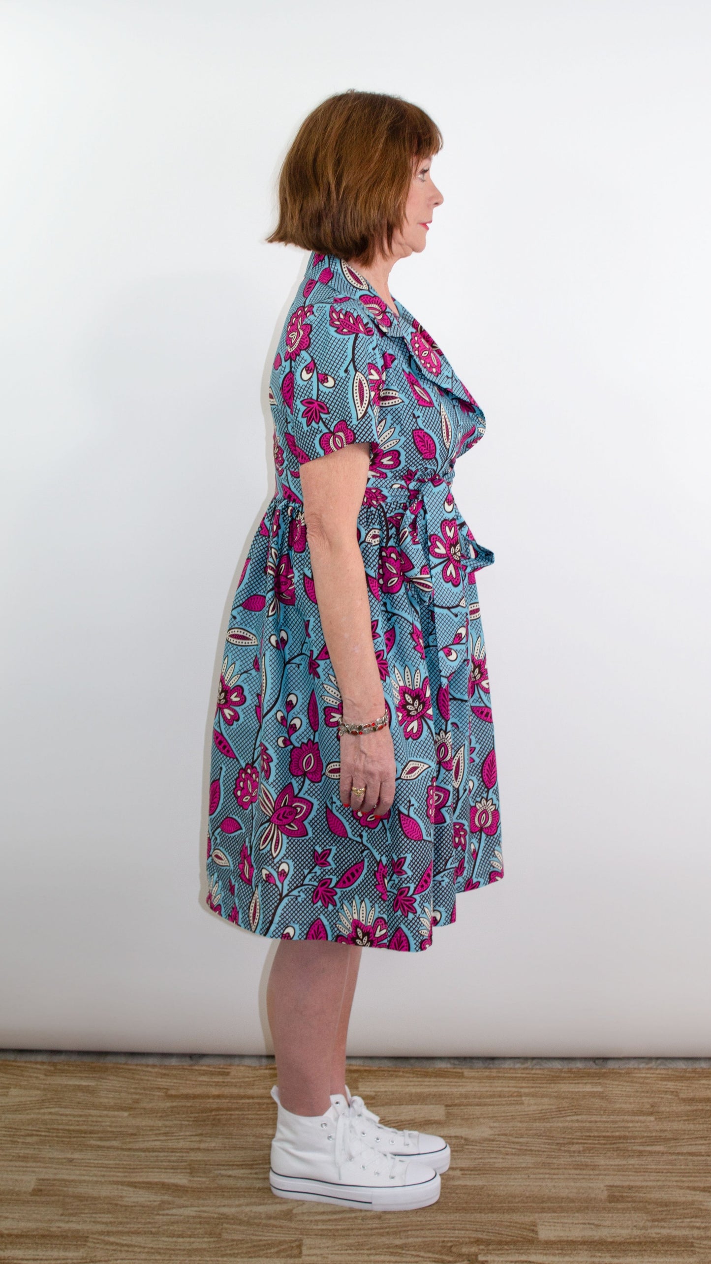 The side of a model showcasing a captivating spring/summer blue print wrap dress with pink floral elements.
