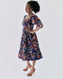 Woman wearing the Amaka Dress, showcasing its vibrant multi-colored smocked bodice and flared midi skirt.