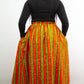 A full-body portrait capturing the back view of a person wearing a striking long orange and yellow skirt with a tie belt, complemented by a black top and stylish black ballet flats. 