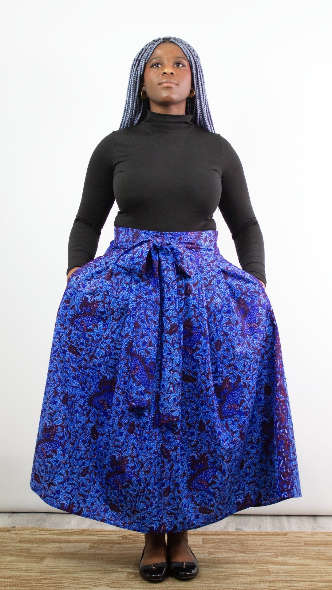 A model with vibrant blue hair striking a pose in a captivating botanical blue skirt, showcasing its volume by placing hands in the pockets and lifting them.