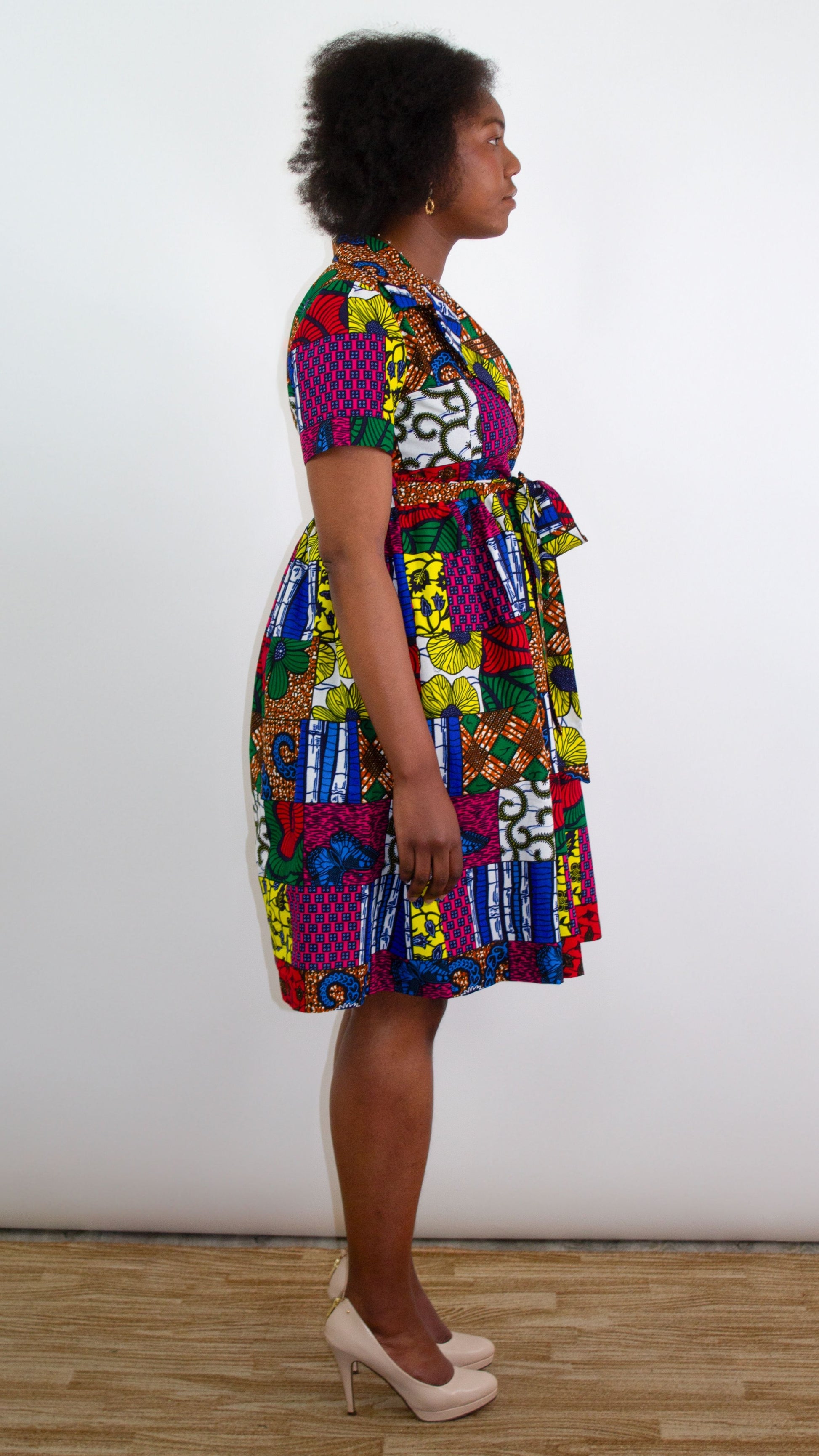 A side view of a model standing gracefully in a patchwork wrap dress, highlighting the tie belt elegantly tied into a beautiful feminine bow. 