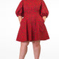 A woman confidently poses with hands in pockets in in a short red print puff-sleeve dress, paired with black heels.